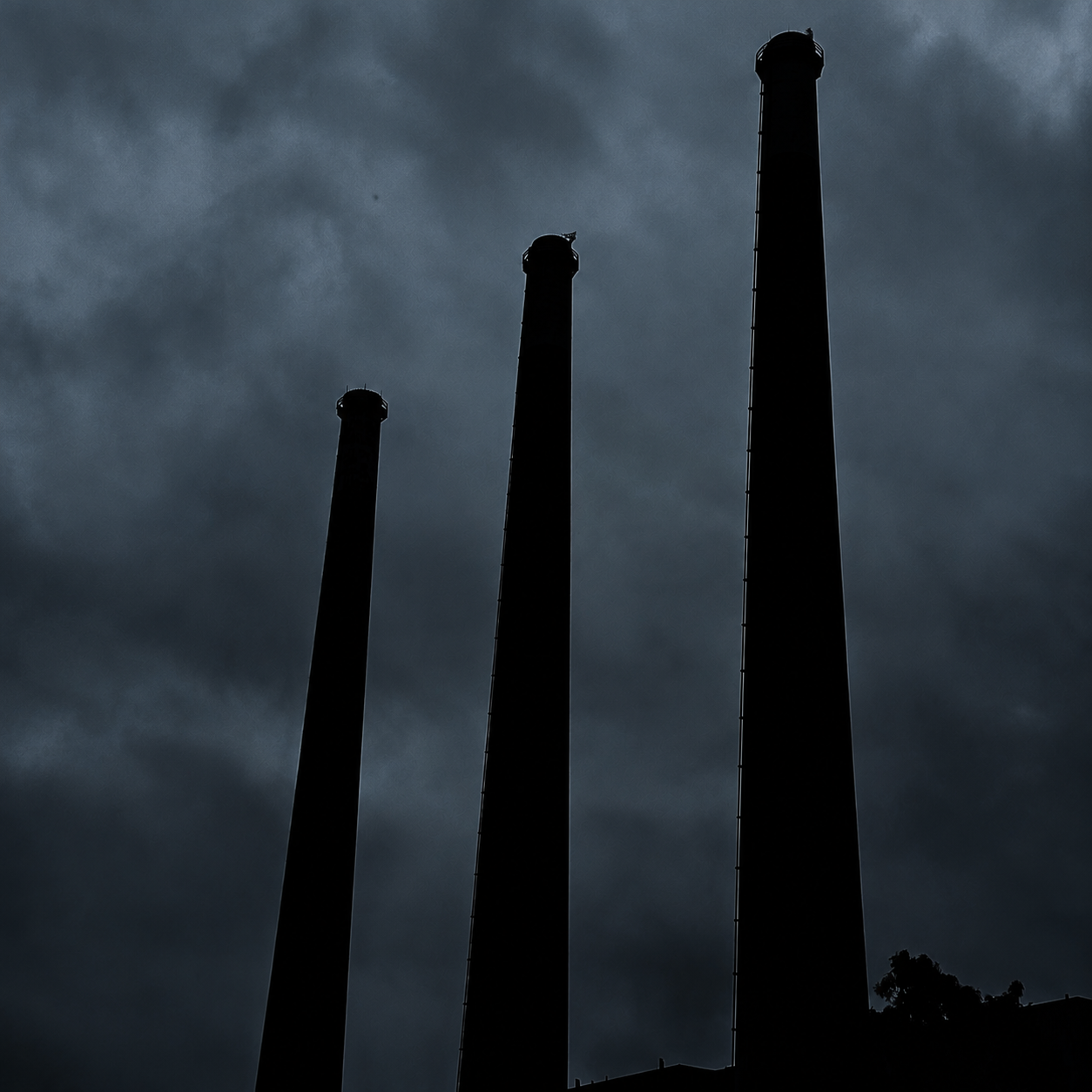 Overcast cover — three smokestacks silhouetted against a heavy sky