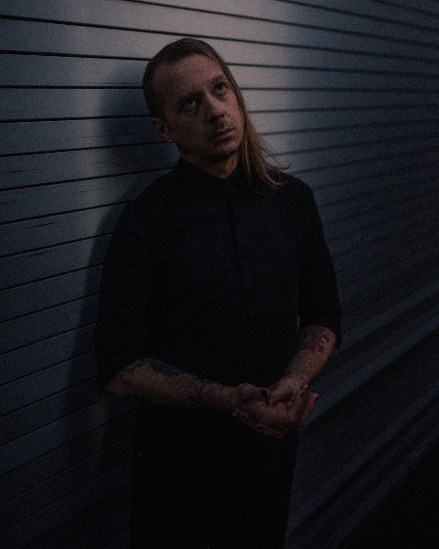 Voidova portrait — leaning against a corrugated metal wall in low blue light